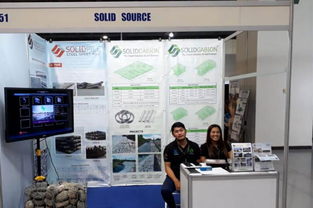 Trade show booth for Solid Source, featuring SolidPile and SolidGabion products, with two people standing behind a table.