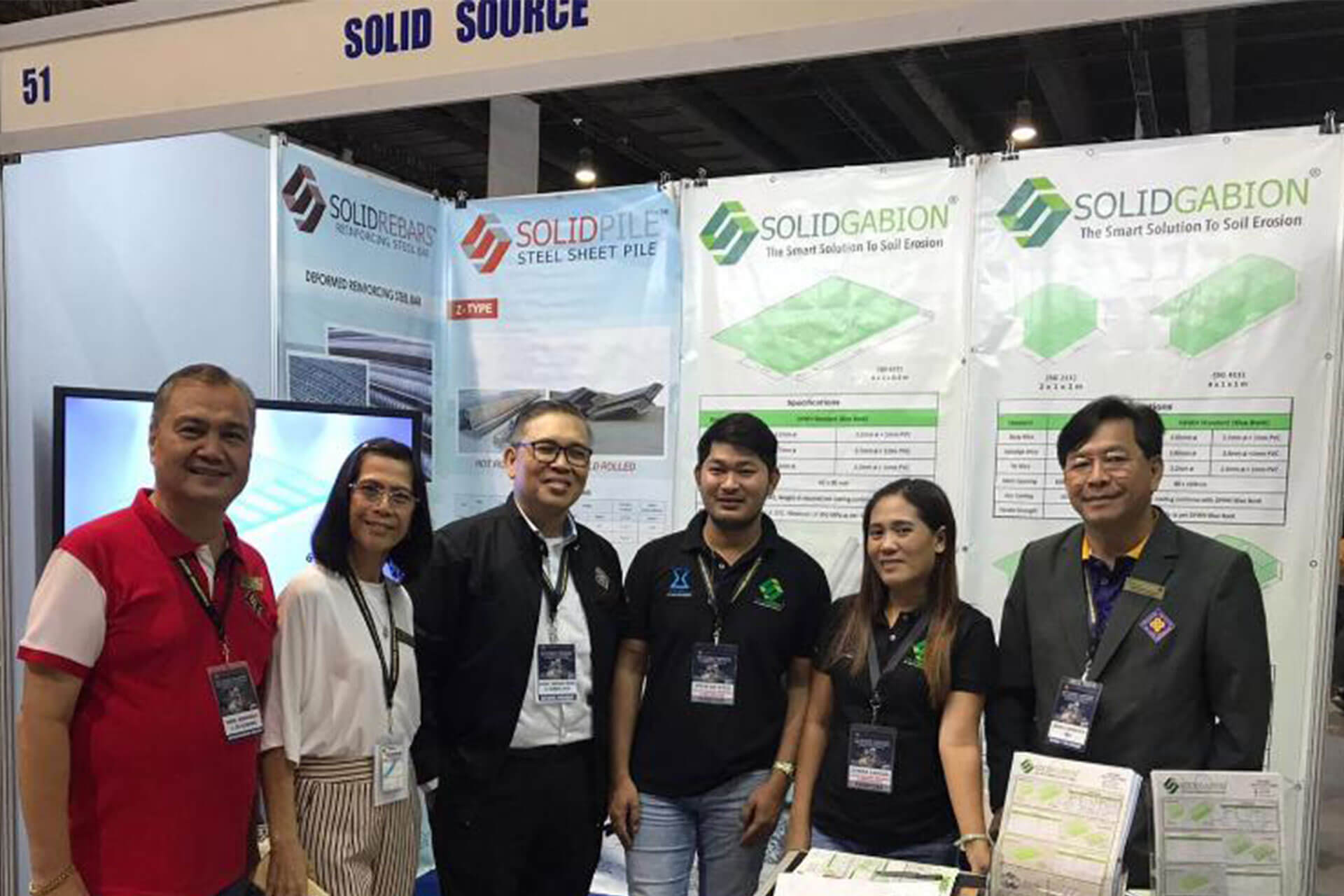 Group of people posing at a "Solid Source" trade show booth featuring "SolidRebars" and "SolidGabion" products.