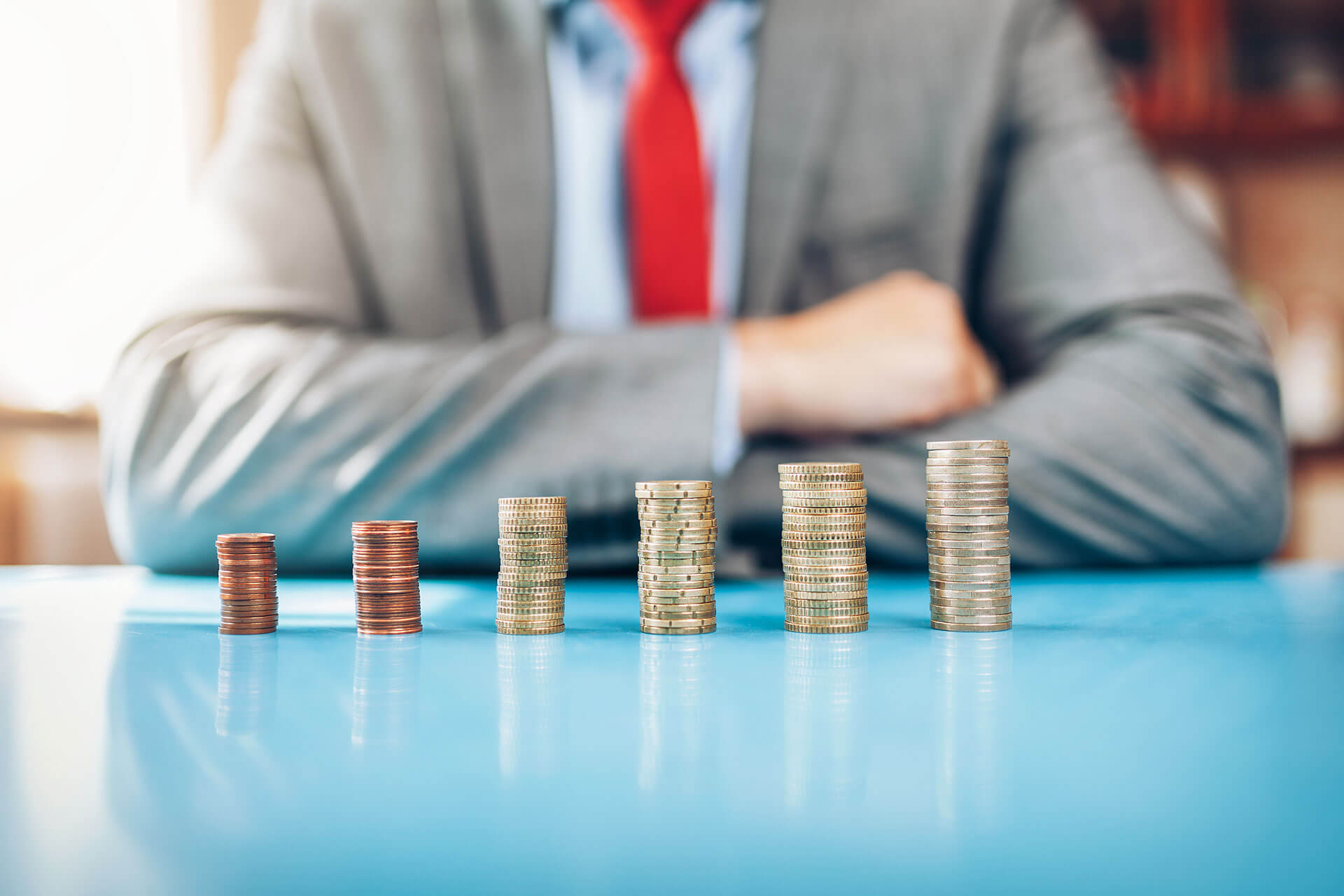 Stacks of coins increasing in height, with a suited man in the background.