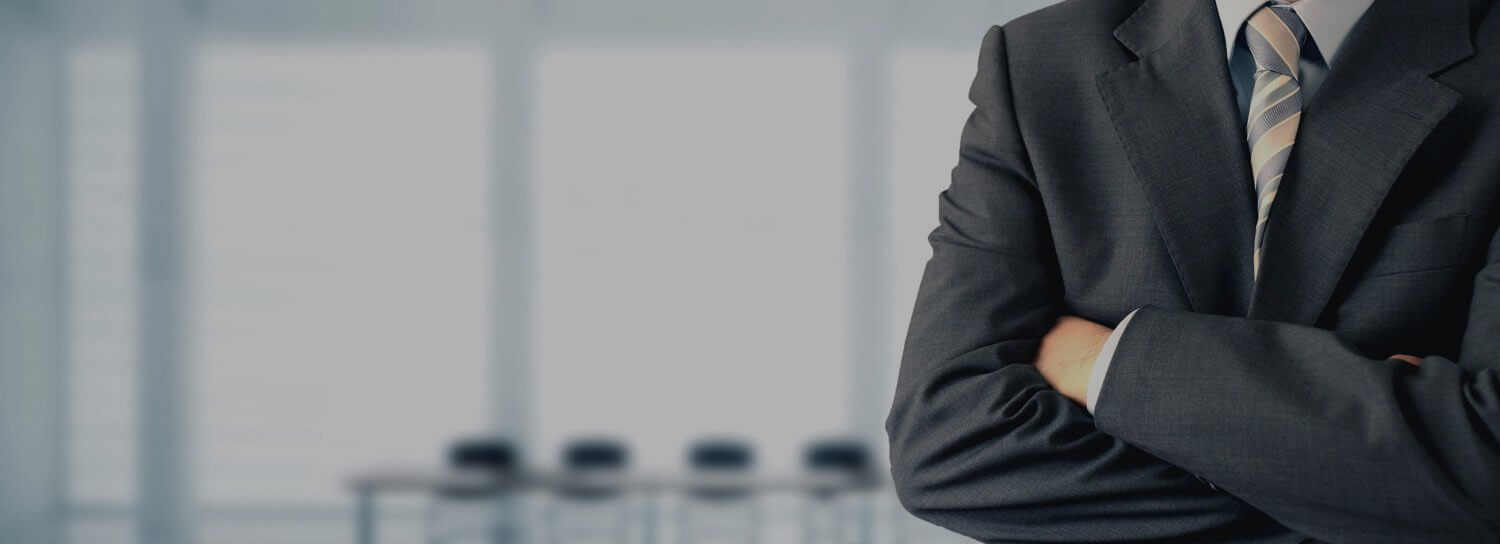 Businessman in suit with arms crossed in office setting.