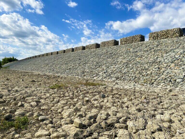 A slope reinforced with rocks and wire mesh under a blue sky.
