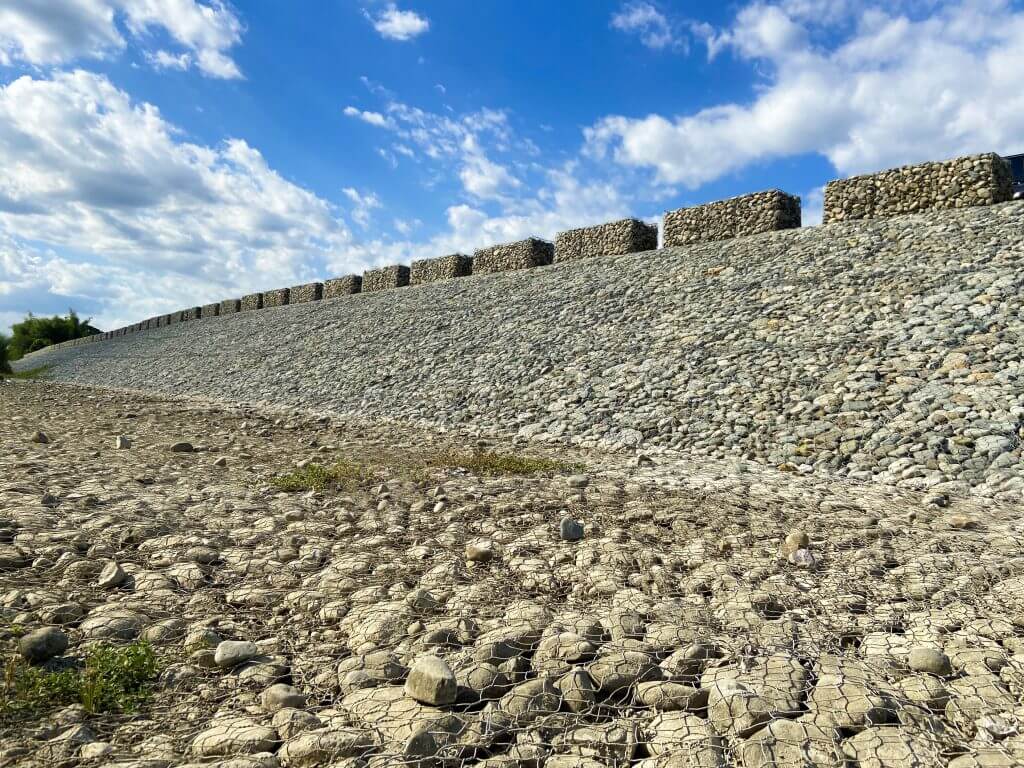 A slope reinforced with rocks and wire mesh under a blue sky.