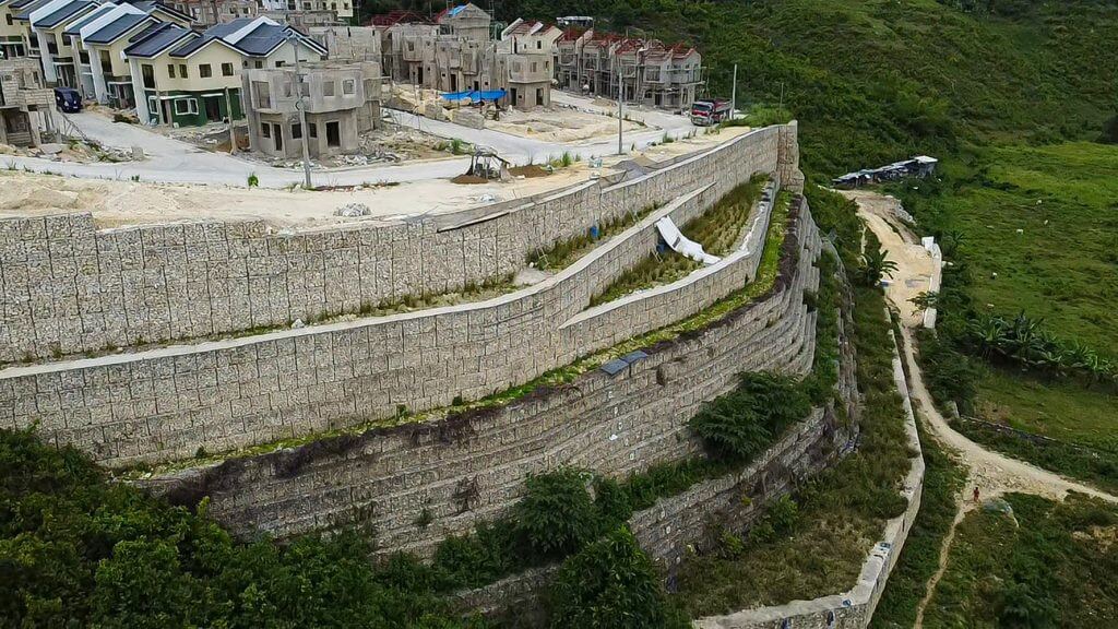 Aerial view of a hillside development with tiered retaining walls and houses under construction.