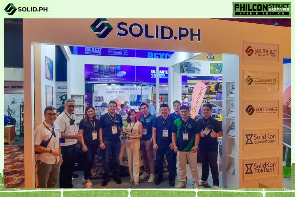 Group of people posing at a SOLID.PH trade show booth with product displays and branding.