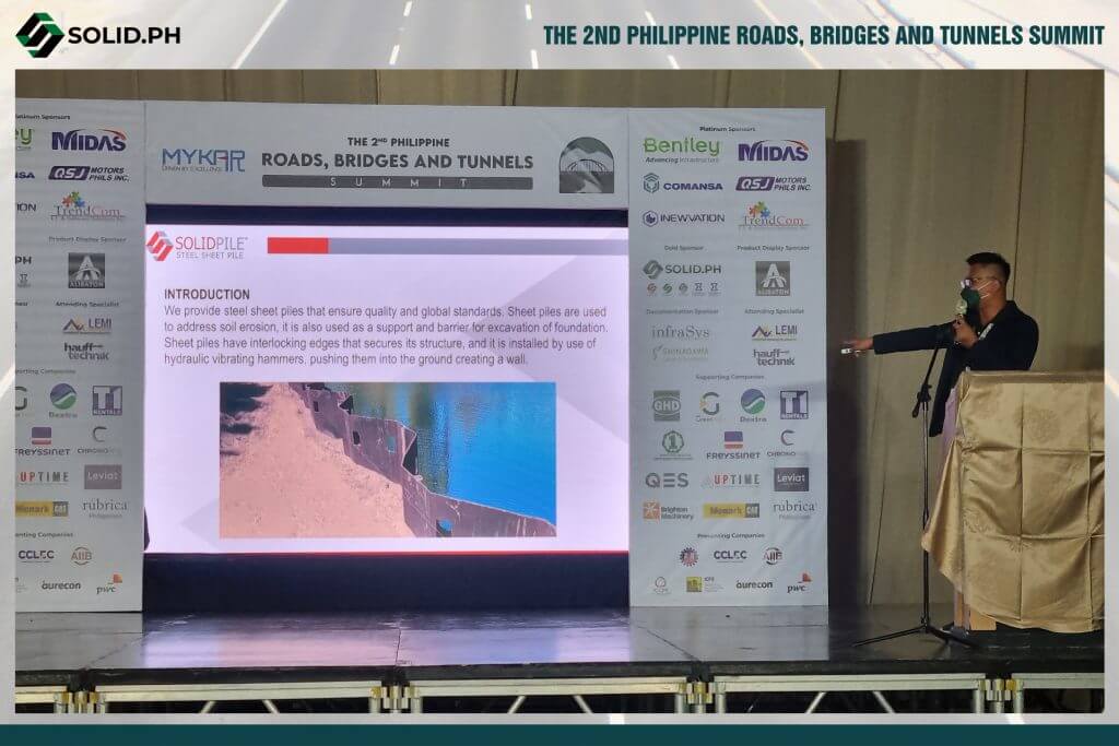 A speaker presents at the 2nd Philippine Roads, Bridges, and Tunnels Summit, with a screen showing information about SOLIDPILE steel sheet piles.