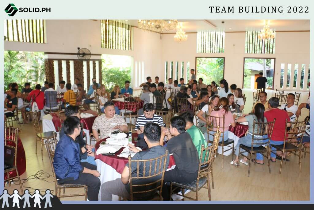 A large group of people seated at round tables in a well-lit room for a team building event.