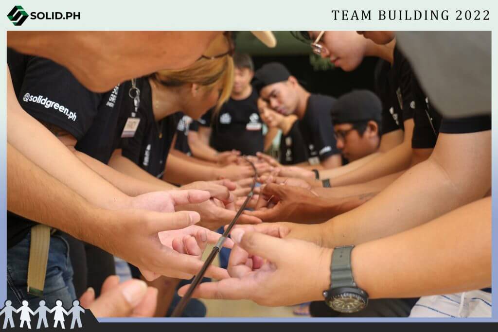 Team building activity showing many hands holding a single rod.