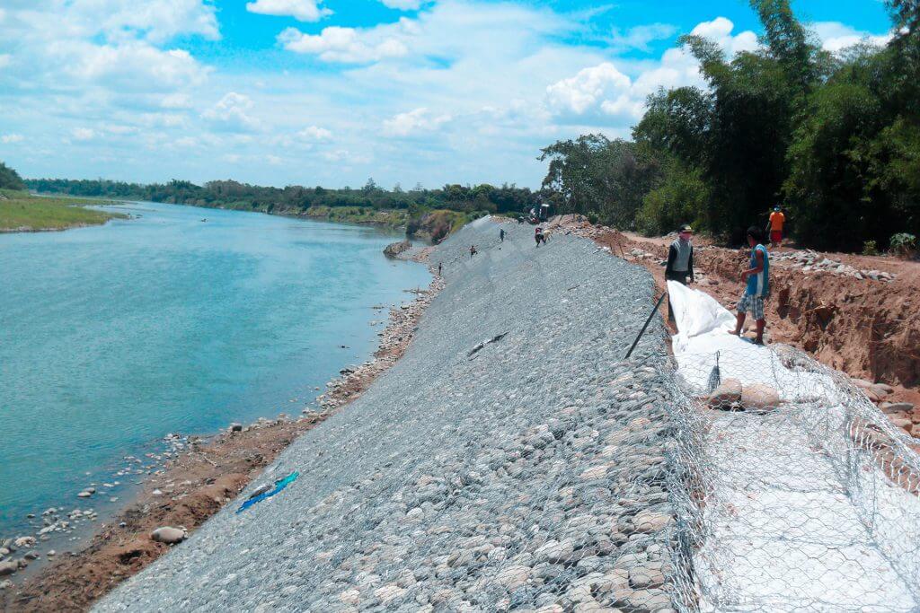 Riverbank erosion control project with gabion walls under construction, workers visible.